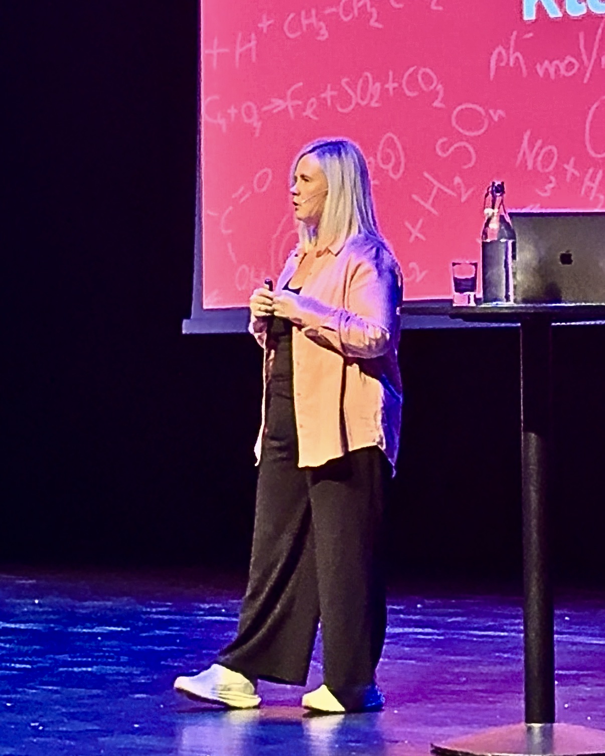 Ingrid Graue Handeland som holder foredrag, rosa bakgrunn og rosa skjorte